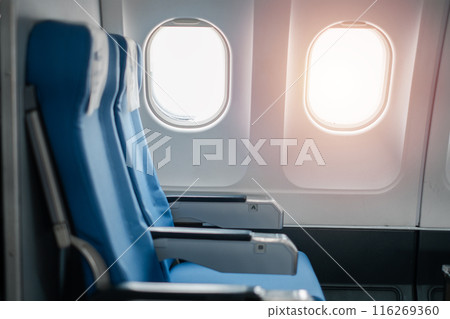 Close-up of empty airplane seats by the window with sunlight streaming through, showcasing a modern aircraft interior. 116269360