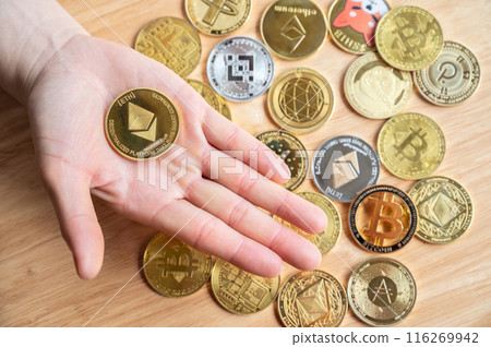 High angle view of person hand holding a Ethereum token with various kinds of cryptocurrency token coins in background. High angle view of person hand holding a Ethereum token with various kinds of cryptocurrency token coins in background. 116269942
