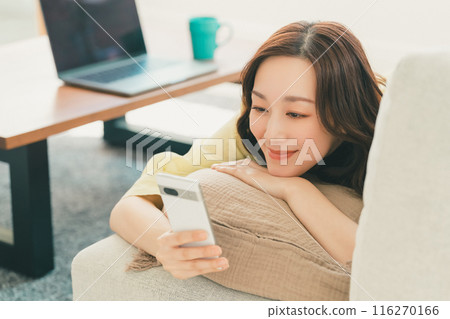 Young woman operating a smartphone on the sofa in the living room 116270166