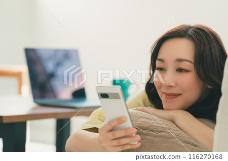 Young woman operating a smartphone on the sofa in the living room 116270168