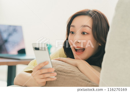 Young woman operating a smartphone on the sofa in the living room 116270169