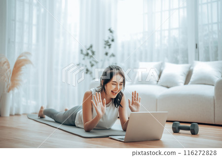 Young Asian woman lying on the floor on yoga mat in front of laptop and training at home Young Asian woman lying on the floor on yoga mat in front of laptop and training at home 116272828