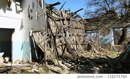 A dilapidated, abandoned building with significant structural damage. Wooden beams and walls have collapsed and debris is scattered on the ground. The surrounding area shows signs of neglect. 116275784