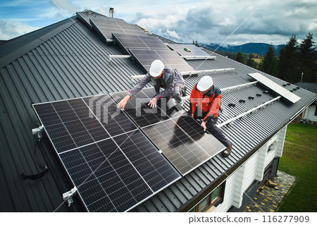 Professional technicians securing heavy solar photovoltaic panels. Male workers installing solar battery on a roof. Concept of green enegry resources. 116277909