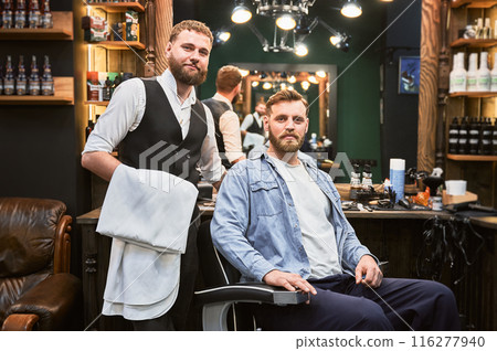 Brutal confident man satisfied with his new look. Experienced barber showing result of his work. Two bearded men smiling to camera. 116277940