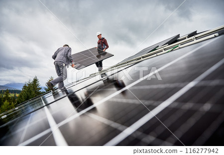 Workers installing solar battery on a roof of house. Male engineers carrying PV panel. Concept of green energetic resources. 116277942