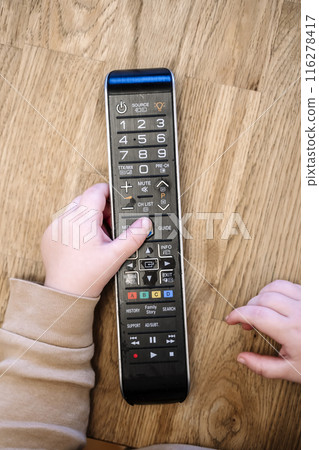 Child is watching TV. A child with a TV remote control in front of the screen. 116278417