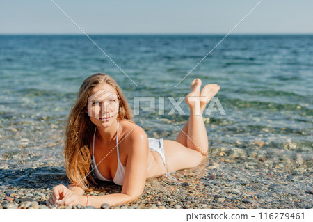 A woman is laying on the beach in a bikini, looking at the camera A woman is laying on the beach in a bikini, looking at the camera 116279461