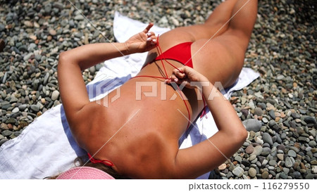 Woman taking red bikini off on beach for tan, lady stripping holiday swimsuit with bow in string. Fun and relax, sexy model untying swimming costume bra, happy woman in swimwear on vacation Woman taking red bikini off on beach for tan, lady stripping holiday swimsuit with bow in string. Fun and relax, sexy model untying swimming costume bra, happy woman in swimwear on vacation 116279550