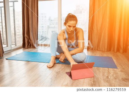 Young athletic attractive woman practicing yoga doing exercises. Works out at home or in a yoga studio, sportswear, blue pants and a full-length top indoors. Healthy lifestyle concept 116279559
