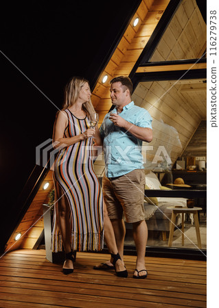 Man embraces his wife while standing on terrace of tiny house late at night 116279738