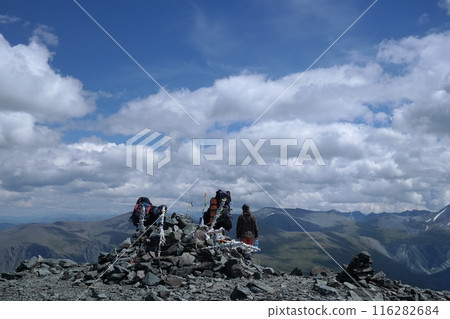 Three hikers on the top of a mountain admiring the view of the valley below them Three hikers on the top of a mountain admiring the view of the valley below them 116282684