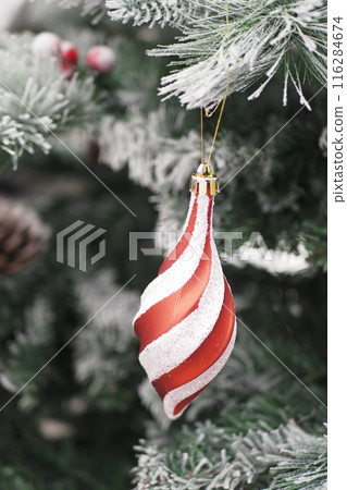 A Red and White Christmas Ornament hangs on a Snowy Tree, symbolizing holiday cheer 116284674