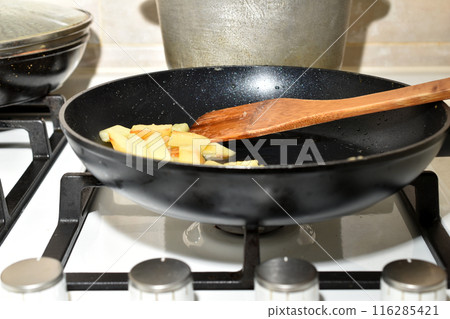 A frying pan with fried potatoes is on the gas stove. 116285421