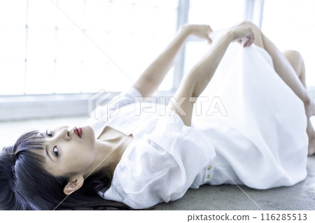 A young woman in a white dress lying down 116285513