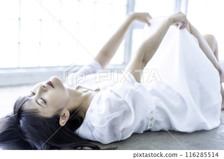 A young woman in a white dress lying down 116285514