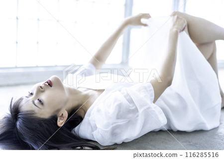 A young woman in a white dress lying down 116285516