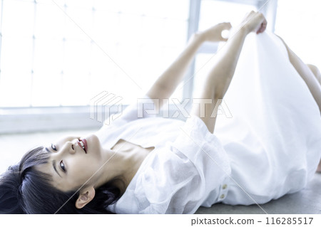 A young woman in a white dress lying down 116285517