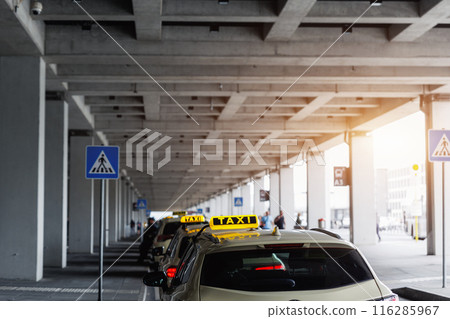 Taxi car Queue yellow taxi symbol on roof stand waiting at parking of airport terminal or railway station Under Concrete Structure Transportation Hub. Urban street transportation comfort service Taxi car Queue yellow taxi symbol on roof stand waiting at parking of airport terminal or railway station Under Concrete Structure Transportation Hub. Urban street transportation comfort service 116285967