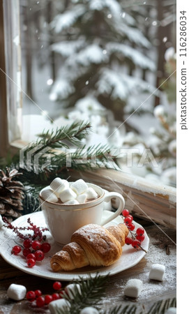 A cup of hot cocoa with marshmallows with a crispy and fresh croissant on a snowy windowsill and a fir branch and cranberries 116286034