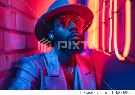 A man wearing a hat and sunglasses leaning against a brick wall. A man wearing a hat and sunglasses leaning against a brick wall. 116286993