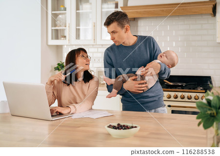 Young family with sleeping infant baby using laptop in the kitchen 116288538