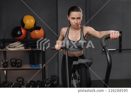 Crossfit female athlete practicing on airbike at gym Crossfit female athlete practicing on airbike at gym 116288595