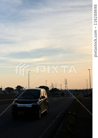 黃昏時分，一輛黑色汽車在路上行駛 116288698