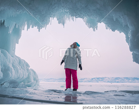 Young woman stands with inside a large ice cave on Lake Baikal during the winter. Young woman stands with inside a large ice cave on Lake Baikal during the winter. 116288827