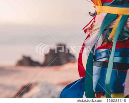 A vibrant bundle of colorful ribbons with blured view of a dramatic rock formation on Olkhon Island in Siberia. 116288848