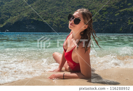 Young woman relaxing on a tropical beach in a red swimsuit Young woman relaxing on a tropical beach in a red swimsuit 116288932