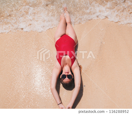 Young woman relaxing on sandy beach in red swimsuit. Top down view. 116288952