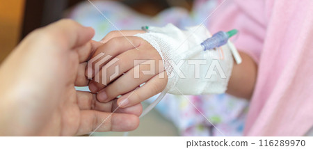 Mother holding child hand with saline IV solution in hospital 116289970