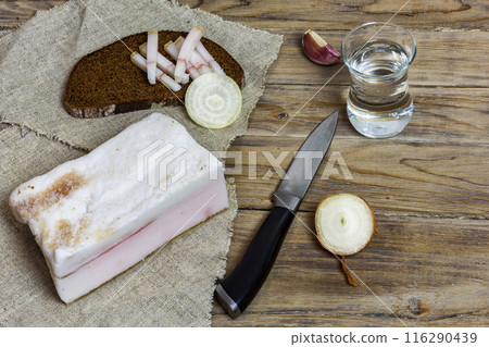 Rustic salted bacon with black bread and a glass of vodka on a wooden surface. On the wooden surface lies rustic salted bacon, black bread, onions and a glass of vodka 116290439