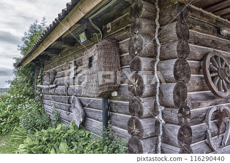 The wall and the corner of a Russian village log hut. Rural architecture. The wall and the corner of a Russian village hut of logs with village utensils The wall and the corner of a Russian village log hut. Rural architecture. The wall and the corner of a Russian village hut of logs with village utensils 116290440