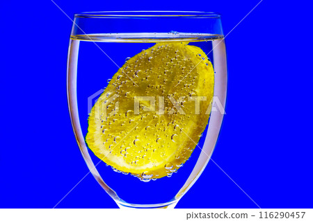 On a blue background, a glass with a lemon covered with gas bubbles. Lemon, covered with bubbles of gas in a glass on a blue blurred background On a blue background, a glass with a lemon covered with gas bubbles. Lemon, covered with bubbles of gas in a glass on a blue blurred background 116290457