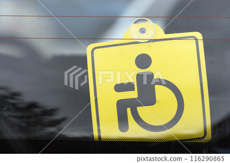 Close-up of a yellow accessible parking permit on a vehicle window indicating special parking rights. 116290865