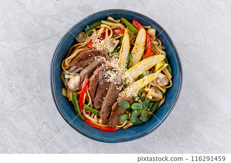 Stir fry noodles with vegetables and beef in blue bowl. Slate background. Close up. Top view. Stir fry noodles with vegetables and beef in blue bowl. Slate background. Close up. Top view. 116291459