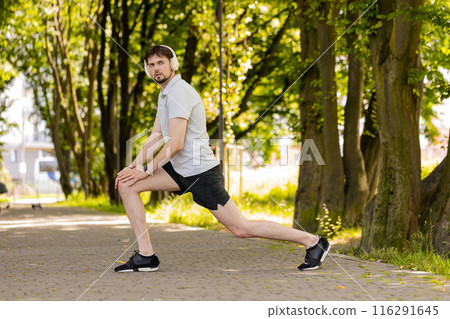 Fitness man in sportswear doing lunges stretching legs on summer park warm up before jogging workout Fitness man in sportswear doing lunges stretching legs on summer park warm up before jogging workout 116291645