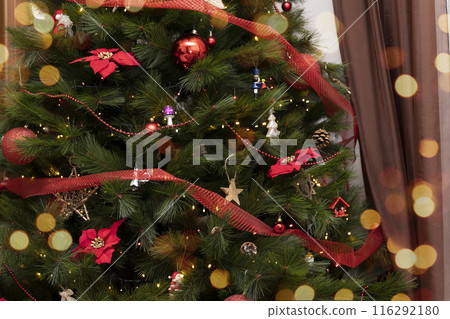 Closeup of christmas tree festively decorated with balls and toys and poinsettia flowers with bokeh 116292180