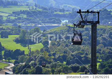 A cable car is suspended above a lush green valley. A cable car is suspended above a lush green valley. 116292201