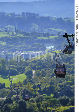 A cable car is suspended above a lush green valley. A cable car is suspended above a lush green valley. 116292212
