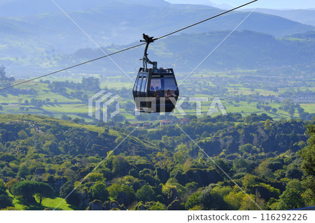 A cable car is suspended above a lush green valley. A cable car is suspended above a lush green valley. 116292226