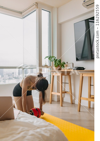 Woman workout exercise with red ab wheel and yellow mat in the room. 116292559