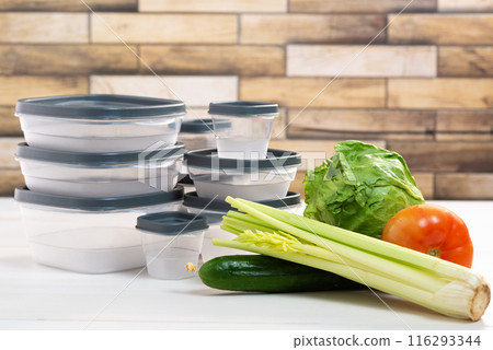 A stack of plastic containers and raw vegetables on the table. Storage for vegetables and fruits in plastic containers 116293344
