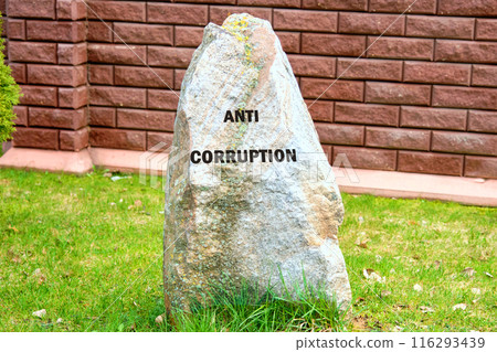 Anti money laundering business and government concept. ANTI CORRUPTION on a stone standing on the grass against the background of a wall, a brick fence 116293439