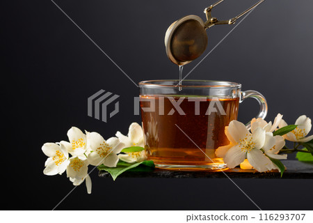 Cup of jasmine tea and fresh jasmine flowers on a black background. Cup of jasmine tea and fresh jasmine flowers on a black background. 116293707