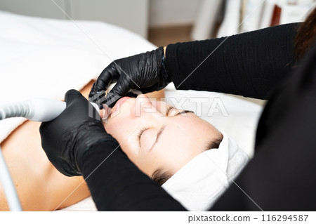 A close-up cosmetologist manipulates a hydropeeling machine to clean and rejuvenate a patient's skin in a modern clinic. A close-up cosmetologist manipulates a hydropeeling machine to clean and rejuvenate a patient's skin in a modern clinic. 116294587