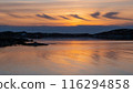 Serene sunset over a calm body of water, with the sky painted in warm hues of orange and yellow 116294858