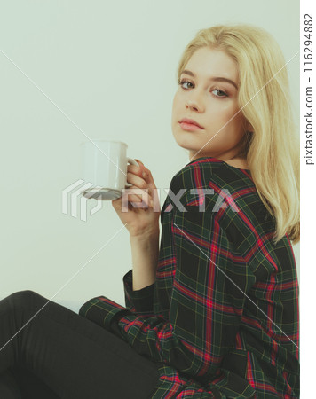 Teenage woman sitting on sofa with mug 116294882